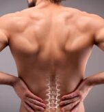 Person with back pain holding lower back, spine illustration visible.