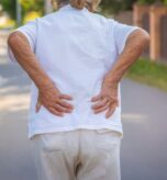 Older person experiencing lower back pain outdoors.