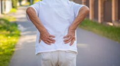 Older person experiencing lower back pain outdoors.