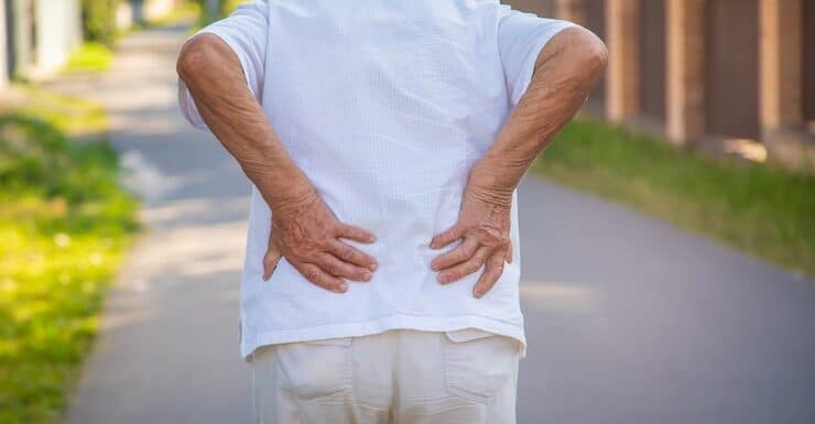 Older person experiencing lower back pain outdoors.