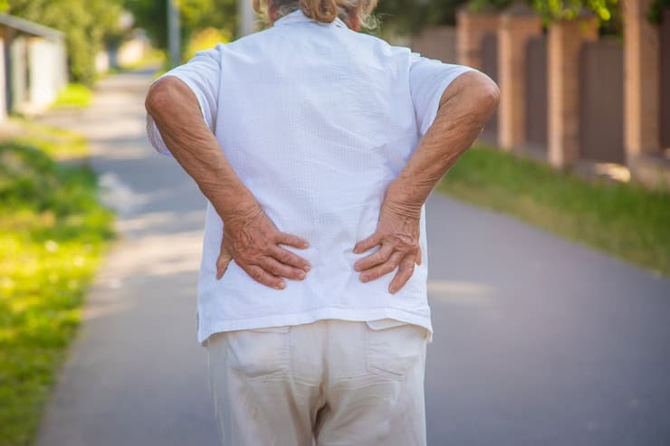 Older person experiencing lower back pain outdoors.