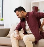 Man experiencing hip pain while sitting on sofa, seeking relief.