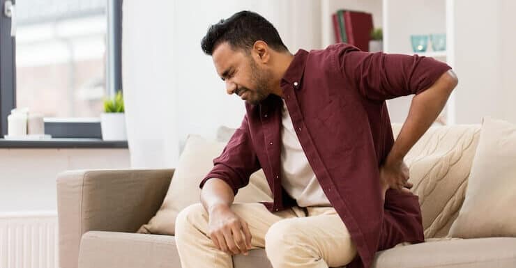 Man experiencing hip pain while sitting on sofa, seeking relief.