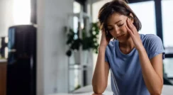 Young woman with migraine pain holding her head in a modern clinic setting.