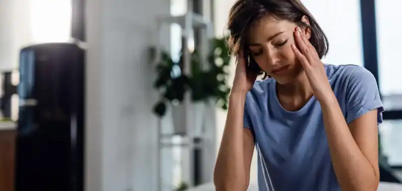 Young woman with migraine pain holding her head in a modern clinic setting.