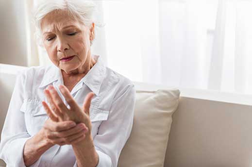 Elderly woman experiencing wrist pain, seeking arthritis treatment.