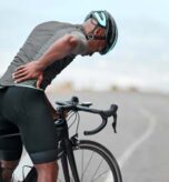 Cyclist holding lower back in pain after long ride on open road.