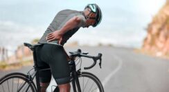 Cyclist holding lower back in pain after long ride on open road.